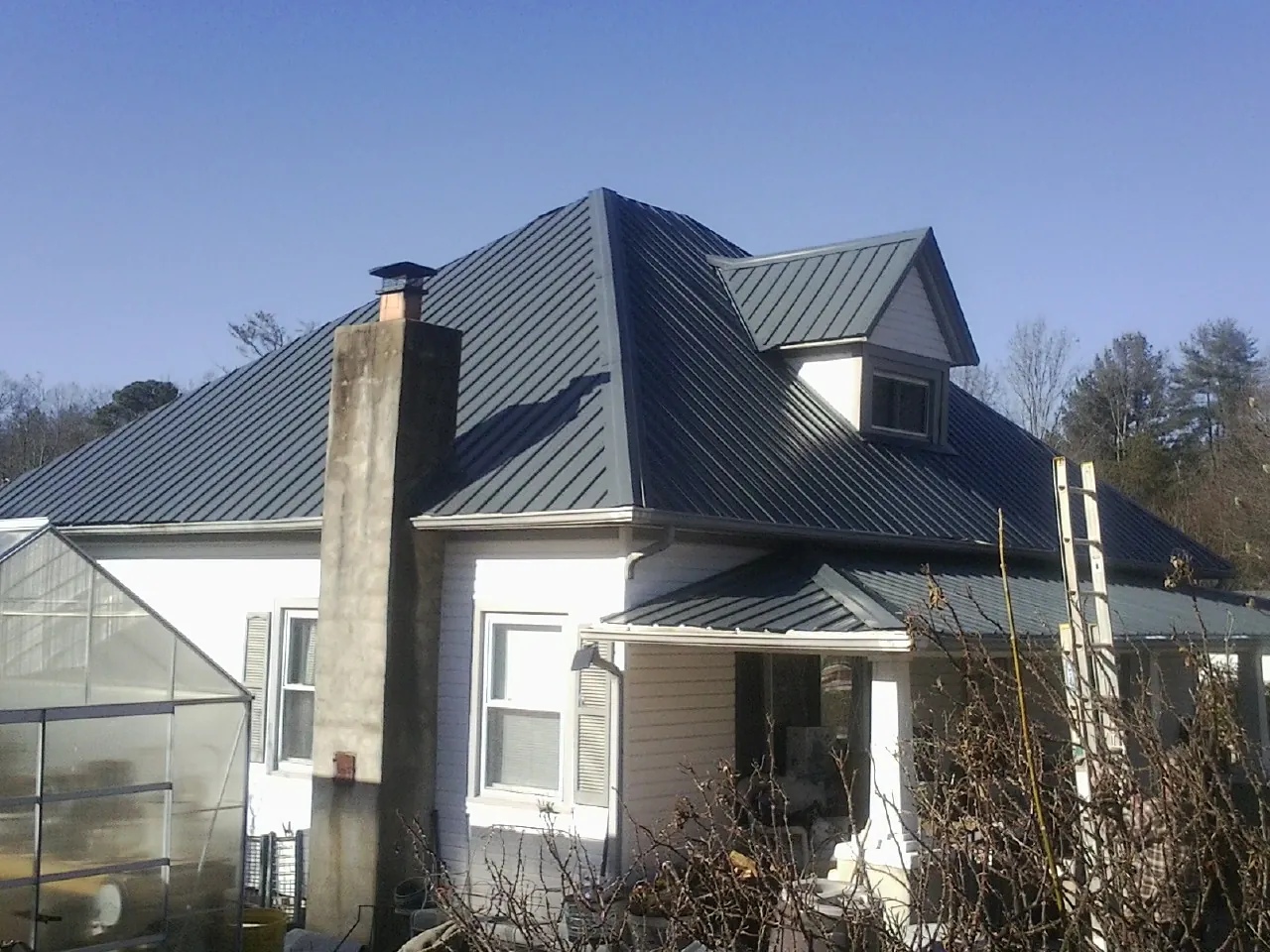 Dark blue standing seam metal roof on a white farmhouse with dormer — Slate & Tile Roof Repair by Roofing Brothers in Russellville