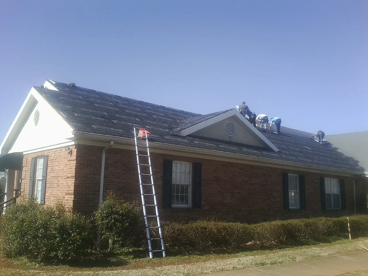 Crew tearing shingles off a brick ranch roof with a ladder set — Emergency Roof Repair work by our crew in Russellville