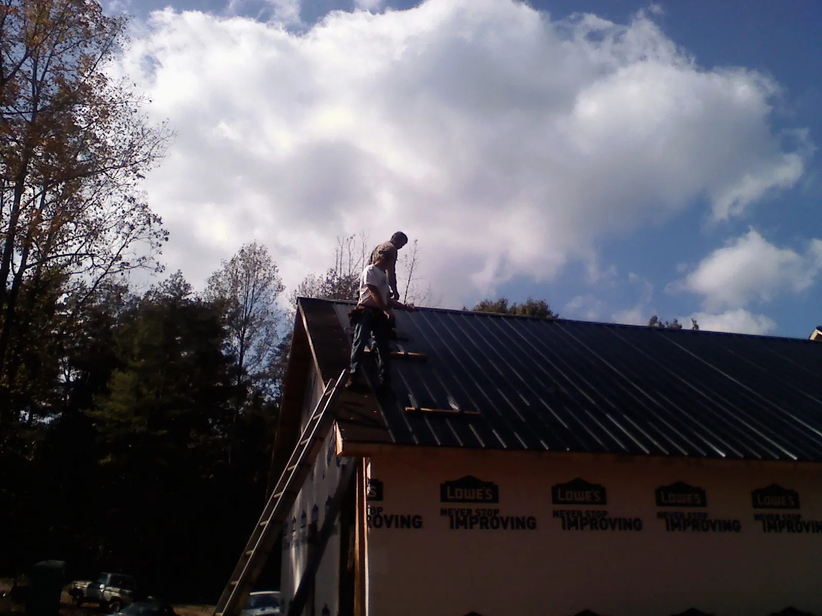 Roofer fastening dark metal panels high against a cloudy sky, from a Roof Inspection job in Russellville